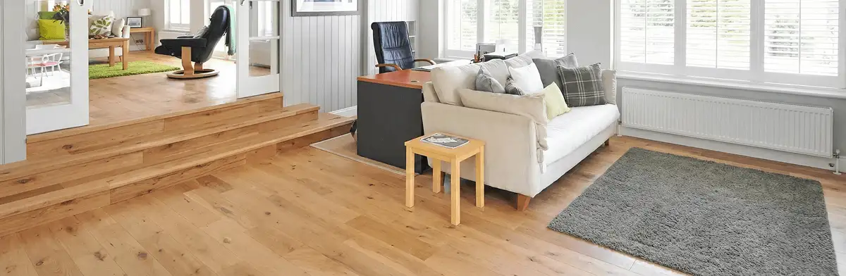A modern living room with professionally installed laminate flooring, a beige sofa, a small side table, a gray rug, and large windows with white shutters in El Paso, TX